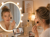 A woman follows a makeup tutorial on her phone while using an EXW 3-in-1 wireless charging station to charge her phone, smartwatch, and earbuds on an organized vanity.